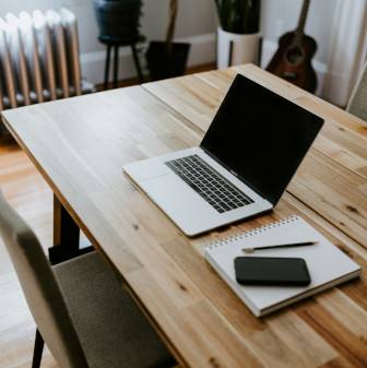 A desk with an open laptop, a notepad, a pen and a phone with an empty chair in front.